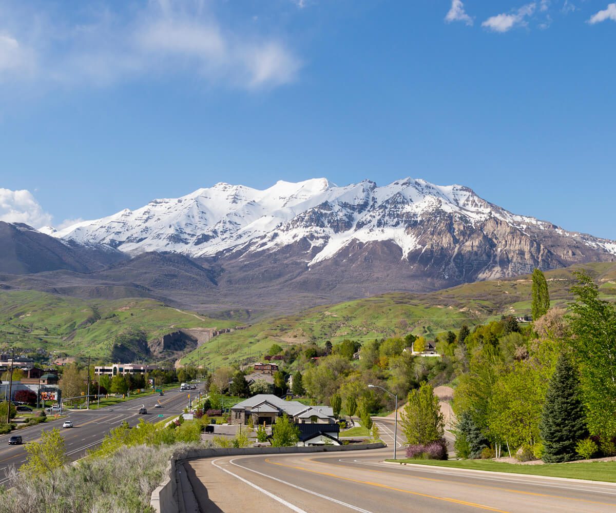Snow-capped mountains with road and greenery.